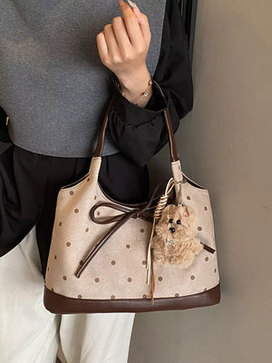 Tan polka dot shoulder bag with brown trim, bow detail, and fuzzy charm.