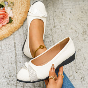 White slip-on wedge flats with rhinestone bow detail.