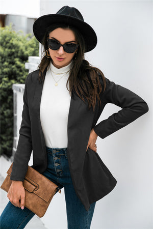Black drape-front blazer with sculpted silhouette and long sleeves, worn open over a white turtleneck.