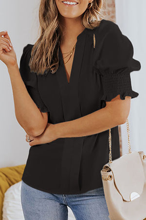 Black puff sleeve v-neck blouse with smocked cuffs and a gold chain detail.