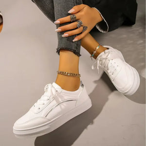 White sneakers with minimalist metallic trim detail and white laces.