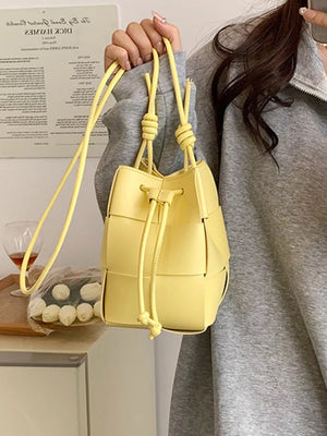 Yellow woven mini bucket bag with drawstring closure and knotted straps.