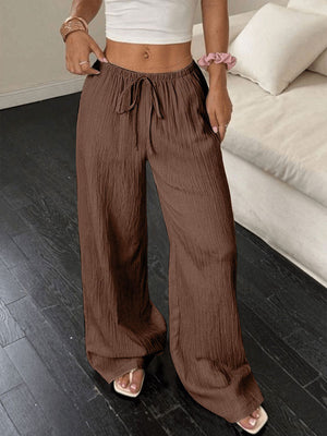 Brown crinkled wide-leg pants with drawstring waist and pockets.
