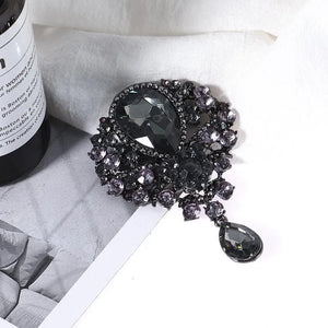 Black teardrop embellished brooch with crystal accents and a dangling pendant.