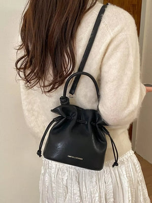 Black pu leather cinch-top crossbody bag with drawstring closure and top handle.