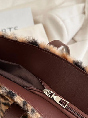 Fuzzy leopard print tote bag with brown faux leather trim and zipper detail.