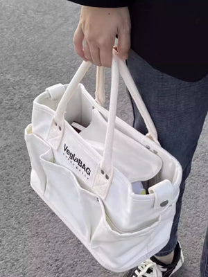 White canvas shopper bag with multiple exterior pockets and rope handles.