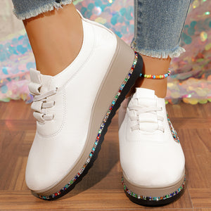 White wedge sneakers with colorful rhinestone embellishments on the sole and side.