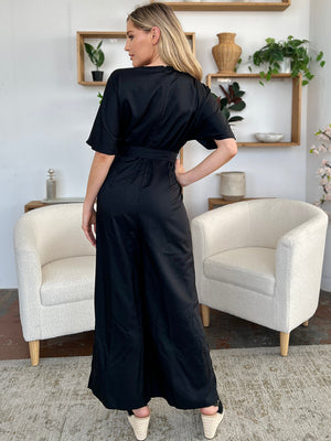 Black wrap jumpsuit with short sleeves, belted waist, and flowing slit legs.