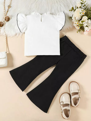 White ruffle-trimmed top with black trim and black flare pants.