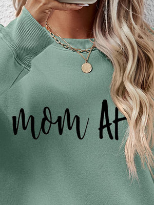 Sage green crewneck sweatshirt with black "mom At" graphic, crew neck, long sleeves, ribbed cuffs and hem.