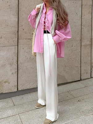 Pink cotton lace-up front relaxed fit shirt with long sleeves, styled with white pants.