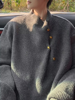 Gray knit sweater with mock neck and gold button accents, ribbed texture.