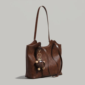 Brown pu leather tote bag with a fuzzy charm and adjustable straps.