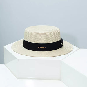Woven straw boater hat in beige with black ribbon band and gold accent.
