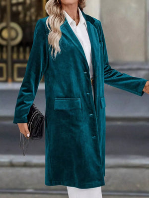 Deep teal velvet longline trench coat with lapel collar and buttoned front, worn with a white shirt.