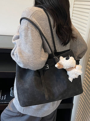 Black shoulder bag with buckle accent and decorative strap, featuring a fluffy charm.