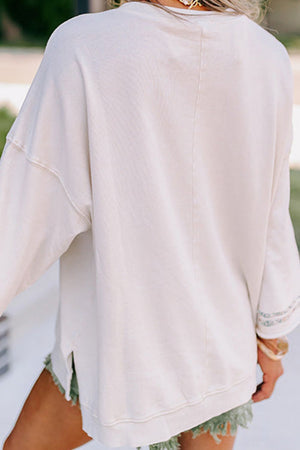 White sweatshirt with floral peace sign detail on sleeve and side slits.