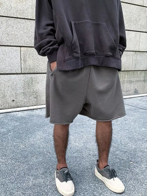 Gray relaxed fit shorts with raw hem, styled with a hoodie and sneakers.