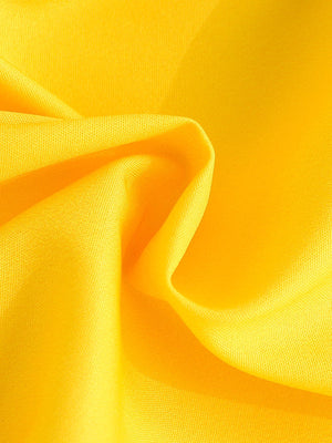 Yellow cotton fabric with soft folds, detail shot of baby outfit material.