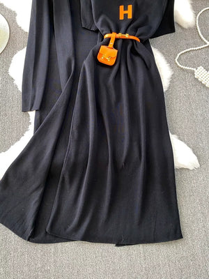 Black knitted maxi dress and cardigan ensemble with orange belt and mini bag detail.