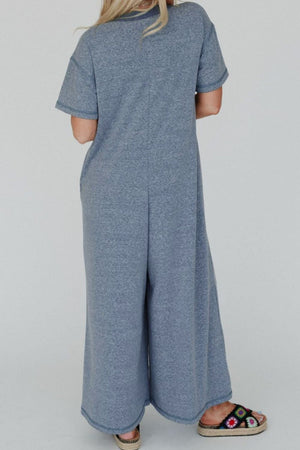 Denim-trimmed wide-leg utility jumpsuit in dusty blue with short sleeves and a relaxed fit.