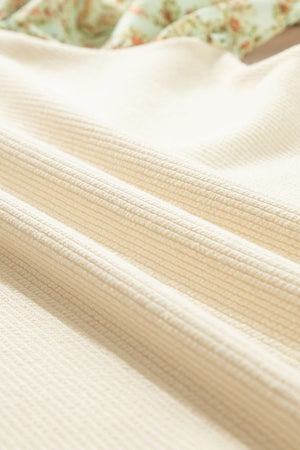 Beige ribbed knit blouse with a floral print detail on the upper portion.