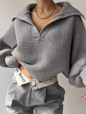 Gray knit sweater with wide collar and balloon sleeves, styled with a gold chain necklace.
