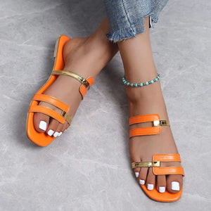 Orange flat slides with gold metallic accent straps and square toe.