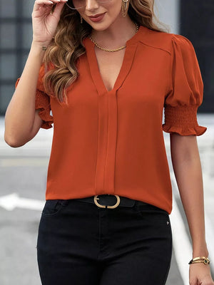Terracotta blouse with notched neckline, puffed sleeves, and smocked cuffs.