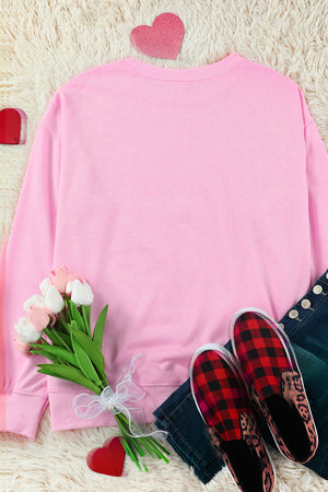 Blush pink crewneck sweatshirt with embellished heart detail, styled with jeans and plaid slip-on shoes.