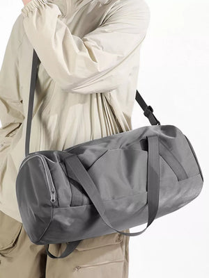Gray barrel duffle bag with zippered pocket and shoulder strap, worn casually.