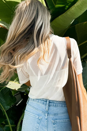 White sheer overlay tee with cami, worn with light wash jeans and a brown bag.