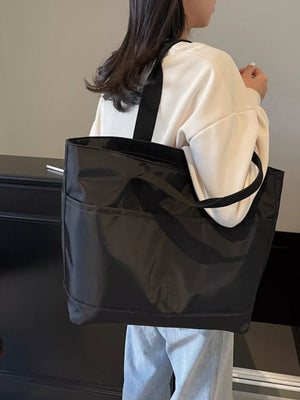 Black Oxford cloth tote bag with exterior pockets and double straps, worn over the shoulder.
