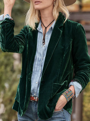 Dark green velvet blazer with rolled cuff detail and buttoned front, styled casually.