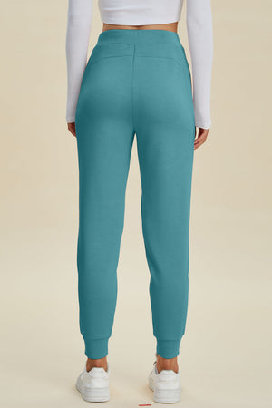 Teal joggers with pockets and cuffed ankles, styled with a white long sleeve shirt and sneakers.