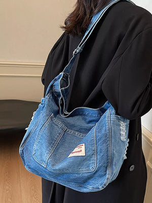 Slouchy blue denim crossbody bag with contrast stitching and distressed details.