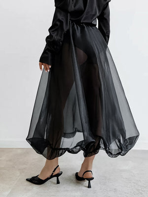 Black midi skirt with sheer overlay and ruffled hem, worn with slingback heels.