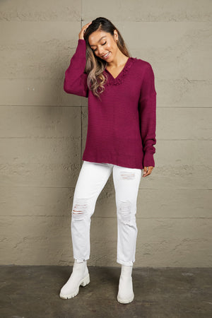 Burgundy knit sweater with V-neck and fringe trim, long sleeves.