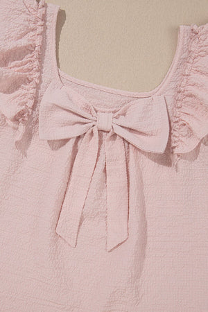 Blush pink textured blouse with ruffle sleeves and a large front bow detail.