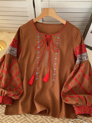 Brown folk-inspired tie neck shirt with red embroidered sleeves and tassels.