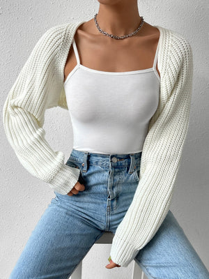 White cropped bolero knit shrug with ribbed sleeves and open front, styled over a camisole and jeans.