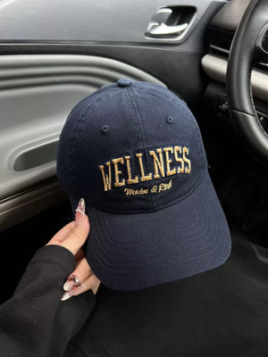 Navy blue cotton baseball cap with gold embroidered WELLNESS and Wisdom & Rich text.