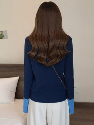 Navy ribbed cardigan with contrast sky blue cuffs and a gold chain strap detail.