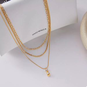 Gold three-layered pendant necklace with mixed chains and a small clear stone accent.