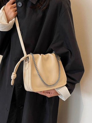 Off-white ruched PU leather crossbody bag with chain detail and knotted strap.