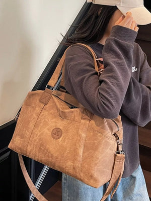 Brown distressed leather travel duffel bag with adjustable strap and exterior pockets.