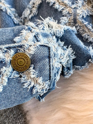 Distressed denim jacket detail with frayed edges and brass button.