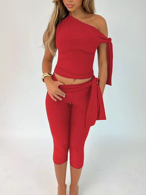 Red asymmetrical one-shoulder top with tie detail and capri pants.