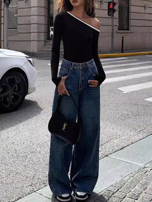 Black off-shoulder ribbed top with contrast trim, long sleeves, paired with wide-leg jeans.